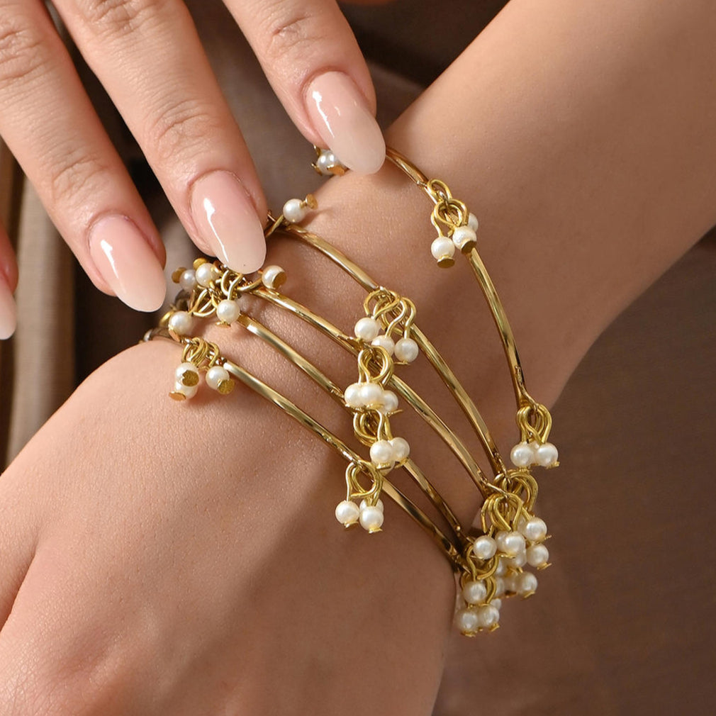 A woman's wrist wearing two gold-plated white pearl drops bangles with a floral design.