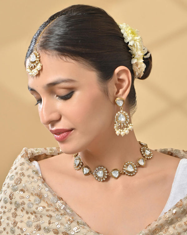 A woman wearing a bridal necklace, earrings, and a maang tikka set with white pearl and kundan studded in gold-plated designs.