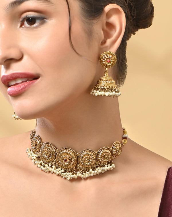 A woman wearing a mehendi gold temple necklace and earrings set with intricate designs and pearl accents.