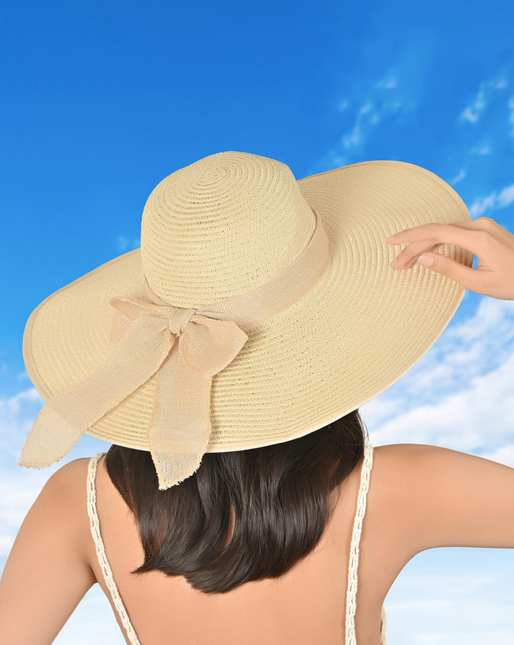 A woman wearing a beige foldable sun hat with a bow on the brim, against a blue sky background.