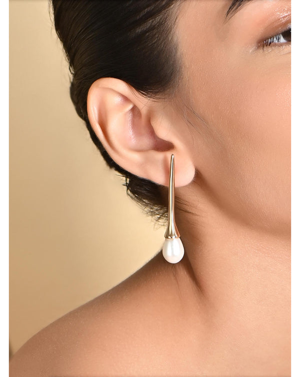 A woman wearing a gold-plated white pearl drop earring.