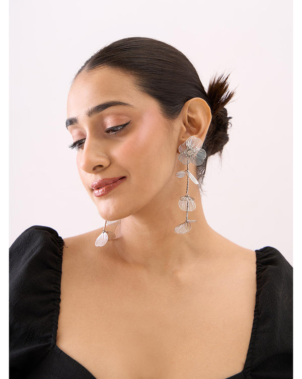 A woman wearing silver floral drop and dangler earrings.