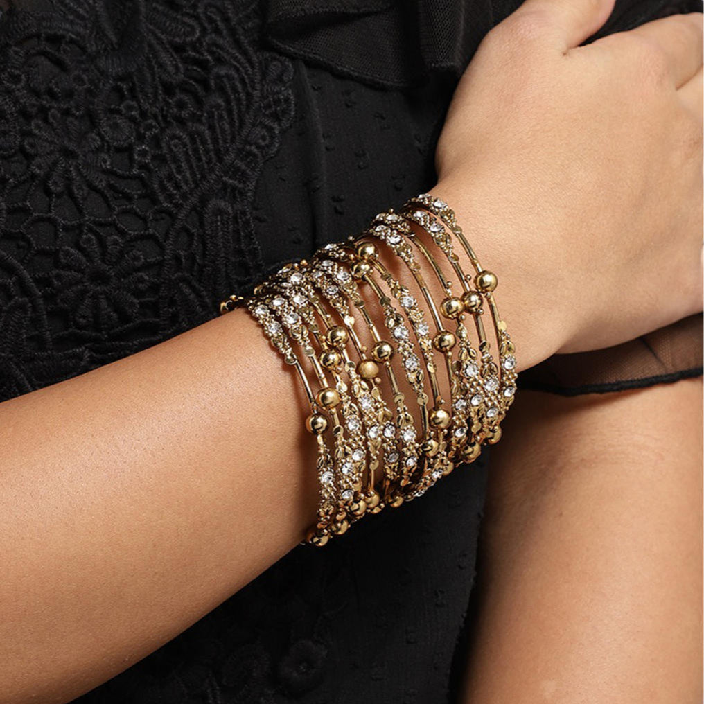 Model wearing Set of 12 gold-plated metal bangles with sparkling stones and beads. Perfect ethnic jewellery for weddings, parties & traditional celebrations.