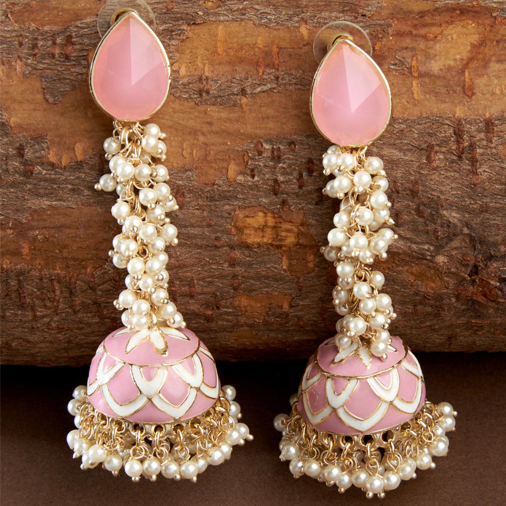 A pair of gold-plated jhumka earrings with pastel pink stones and beads embellished throughout, displayed against a wooden backdrop.