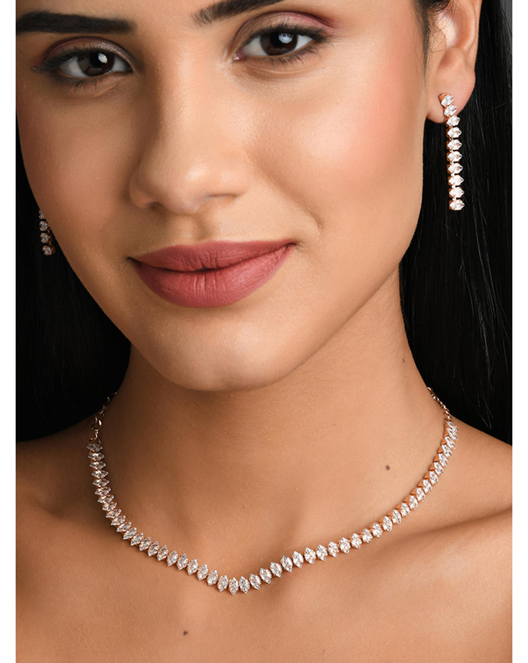 A model wearing a rose gold plated necklace and earrings jewellery set with intricate motifs and American Diamond stones.