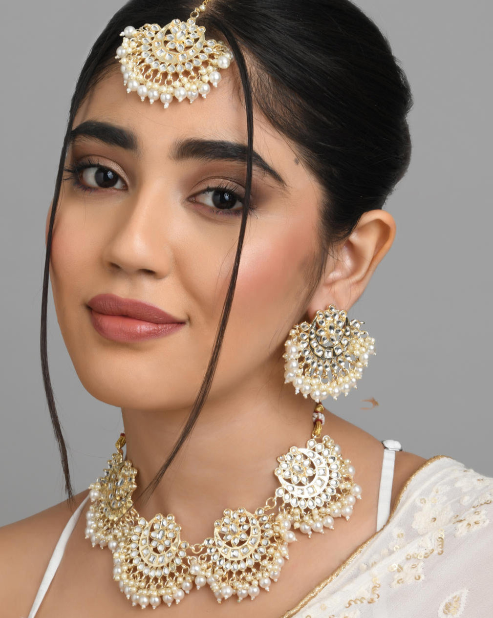 A woman wearing a traditional Indian ethnic gold and white pearl kundan choker necklace, earrings, and maang tikka set.
