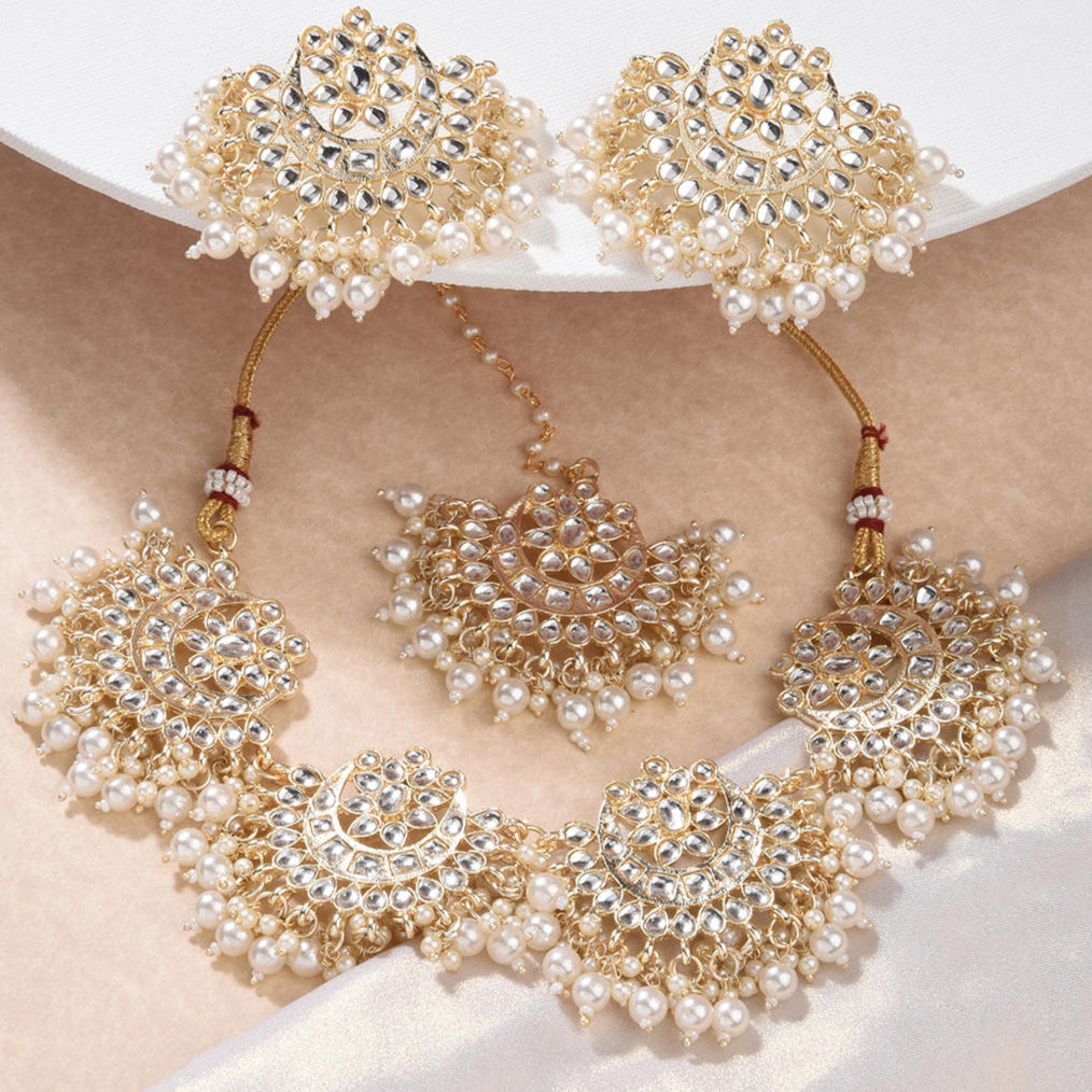 a traditional Indian ethnic gold and white pearl kundan choker necklace, earrings, and maang tikka set.