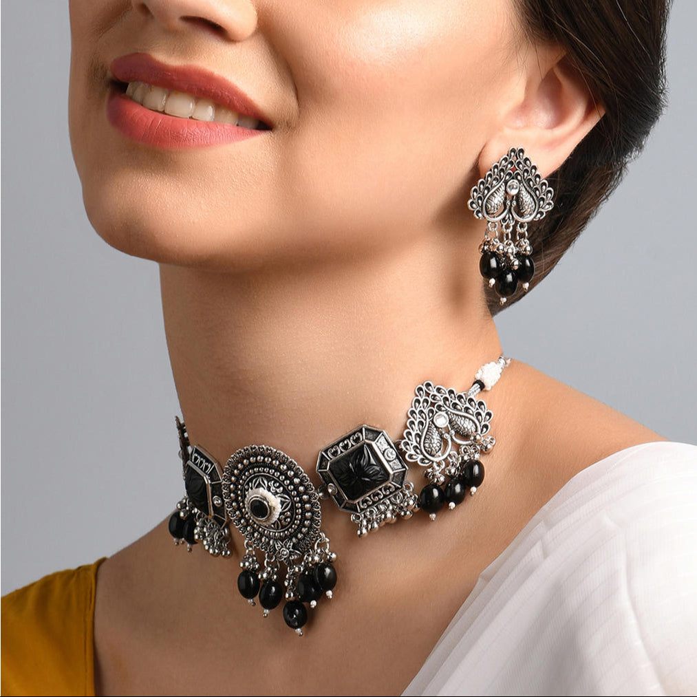 A woman wearing a silver-plated oxidised black beaded peacock jewelry set which includes a necklace and a pair of earrings.