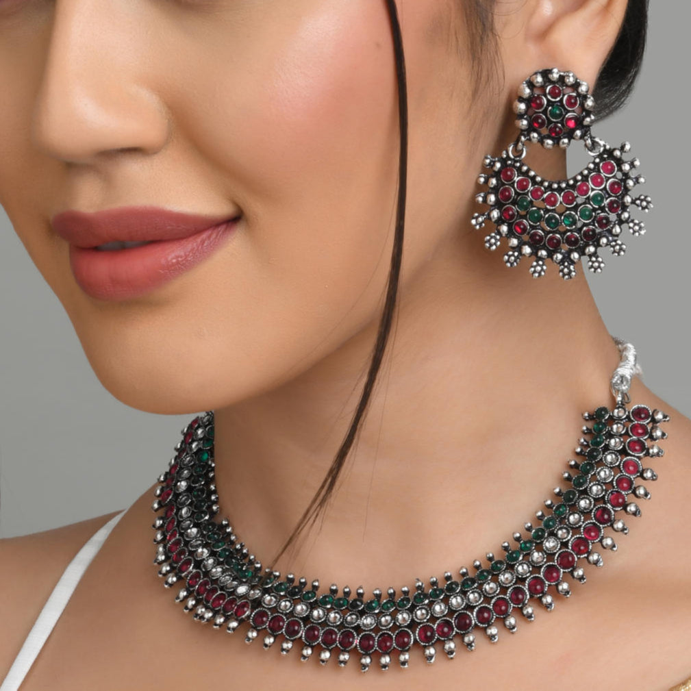 A woman wearing a traditional south Indian silver choker necklace with maroon and green pearl embellishments and matching earrings.
