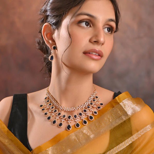 a luxurious bridal jewellery set which includes a necklace, earrings, and maang tikka, featuring blue sapphire stones and gold-tone metal.