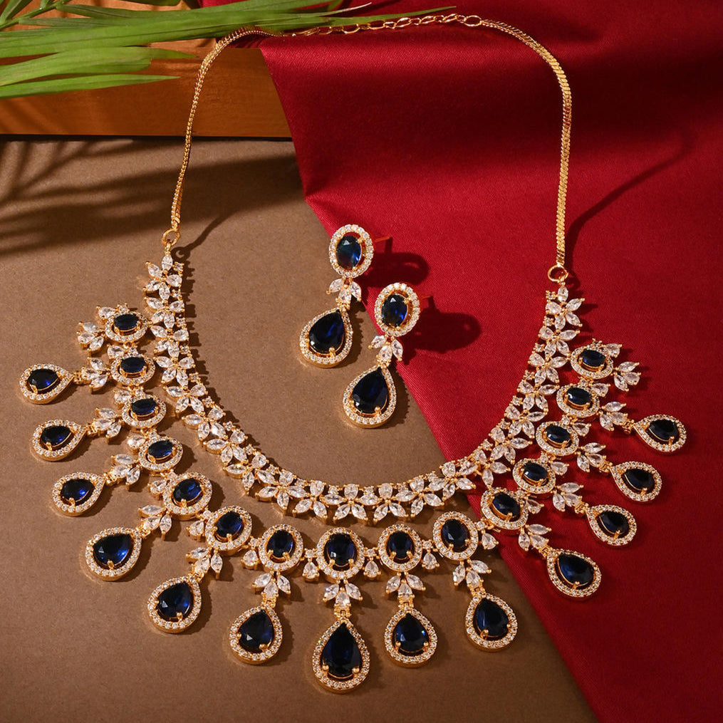a luxurious bridal jewellery set which includes a necklace, earrings, and maang tikka, featuring blue sapphire stones and gold-tone metal.