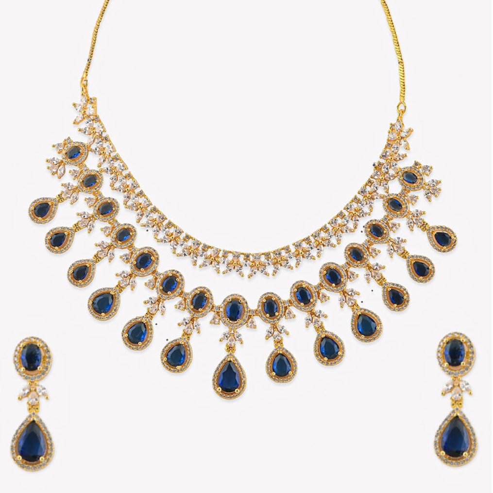 a luxurious bridal jewellery set which includes a necklace, earrings, and maang tikka, featuring blue sapphire stones and gold-tone metal.