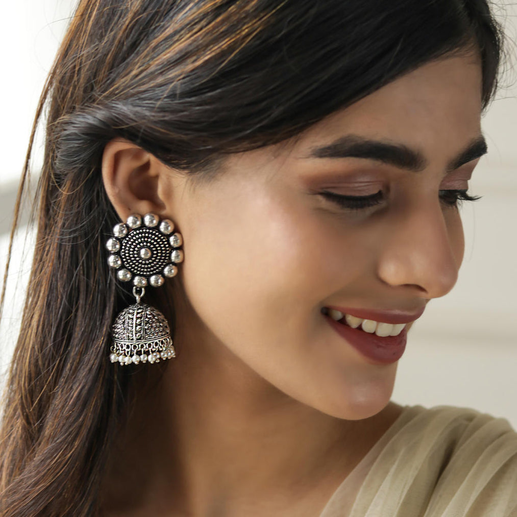 A woman wearing a silver oxidized matte finish floral jhumka earring.