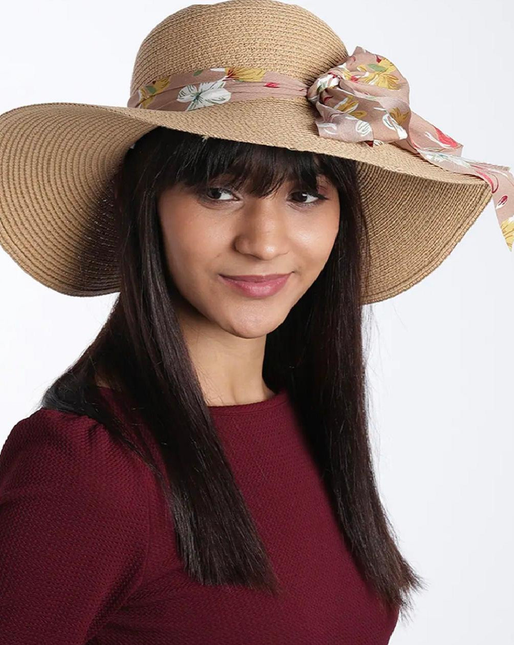 A woman wearing a beige beach hat with a soft brown multicolor floral printed scarf around the base.