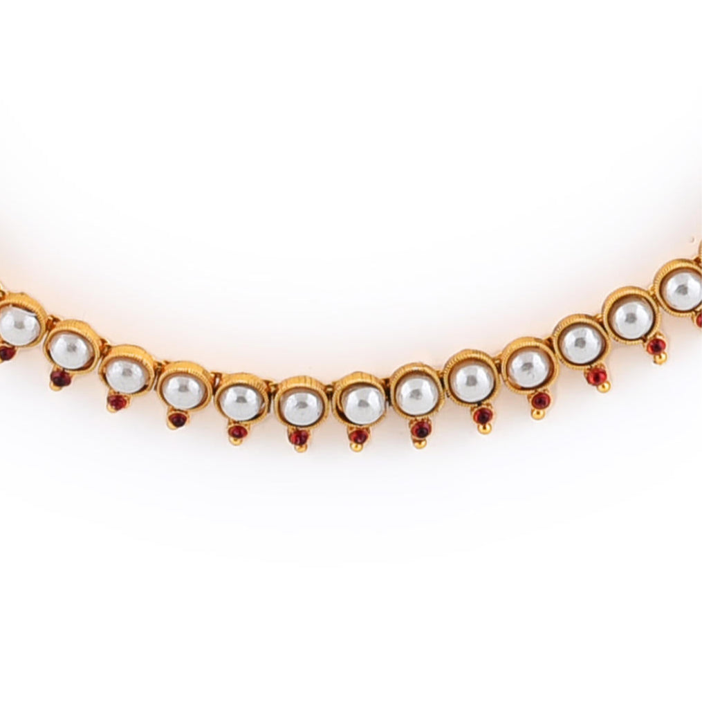 a gold-plated necklace and earrings set with white pearls and fuchsia stones close up.