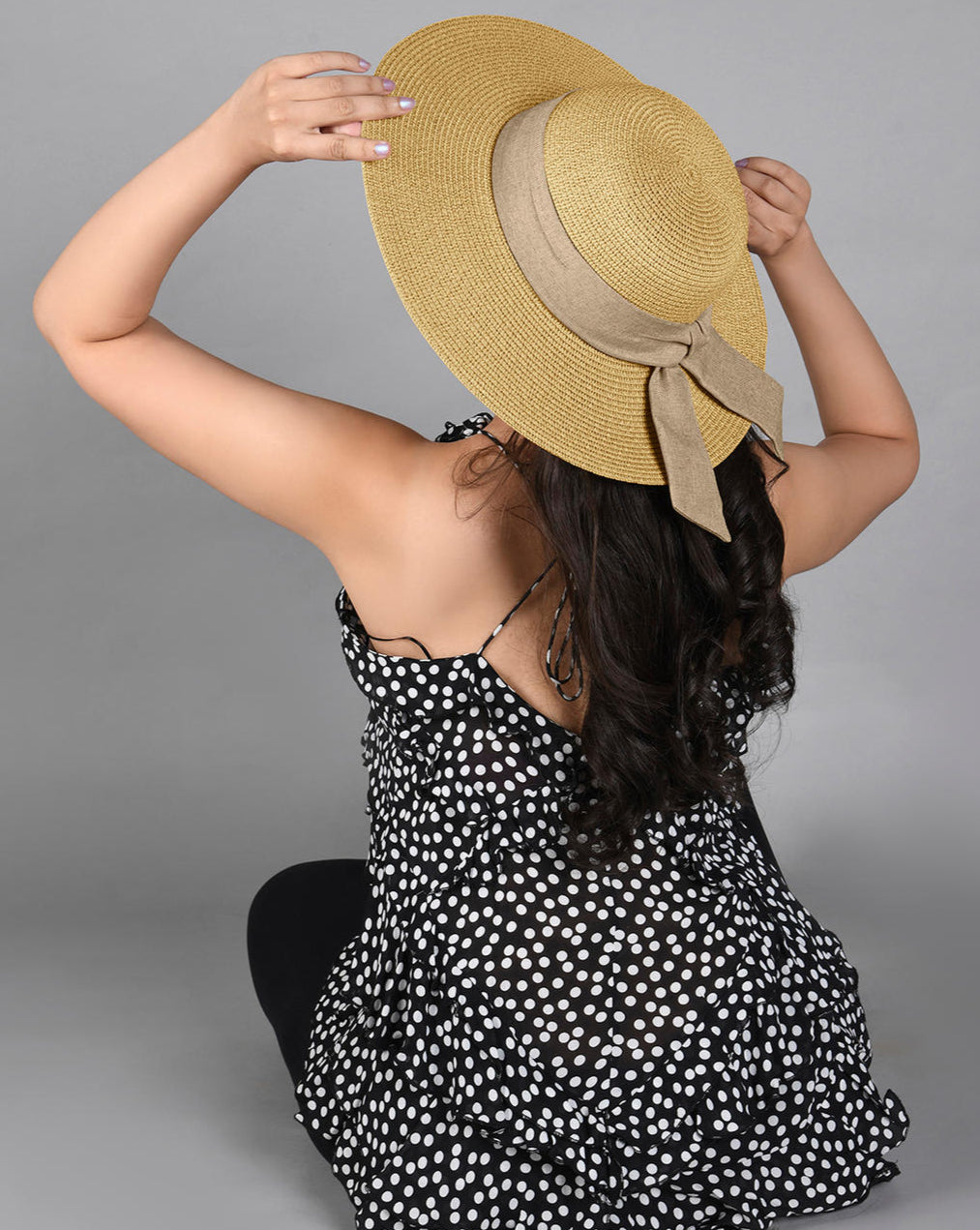 A beige beach hat made from papyrus with a khaki scarf tied around the base.