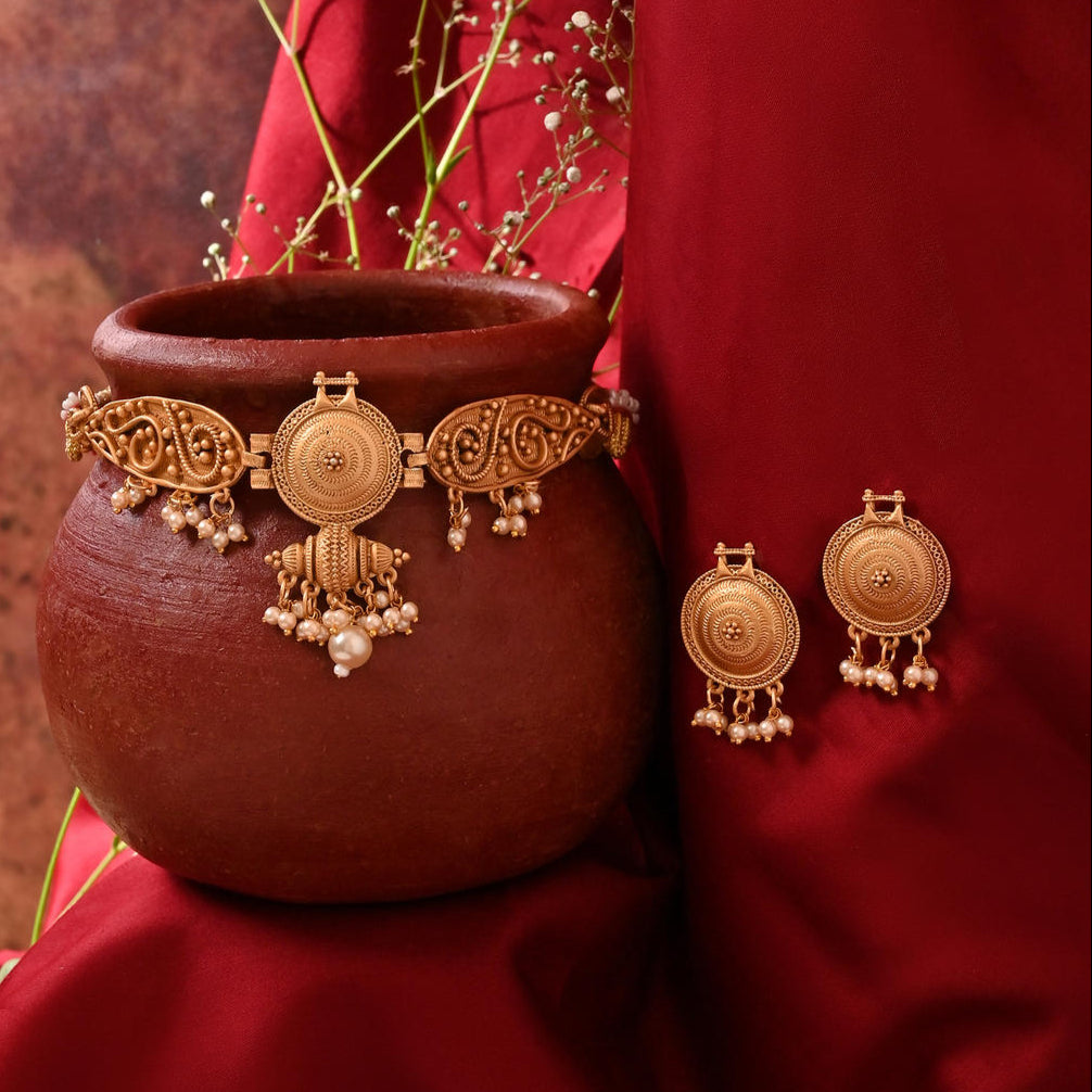 a gold-plated choker necklace with intricate designs and pearl accents, paired with matching earrings.