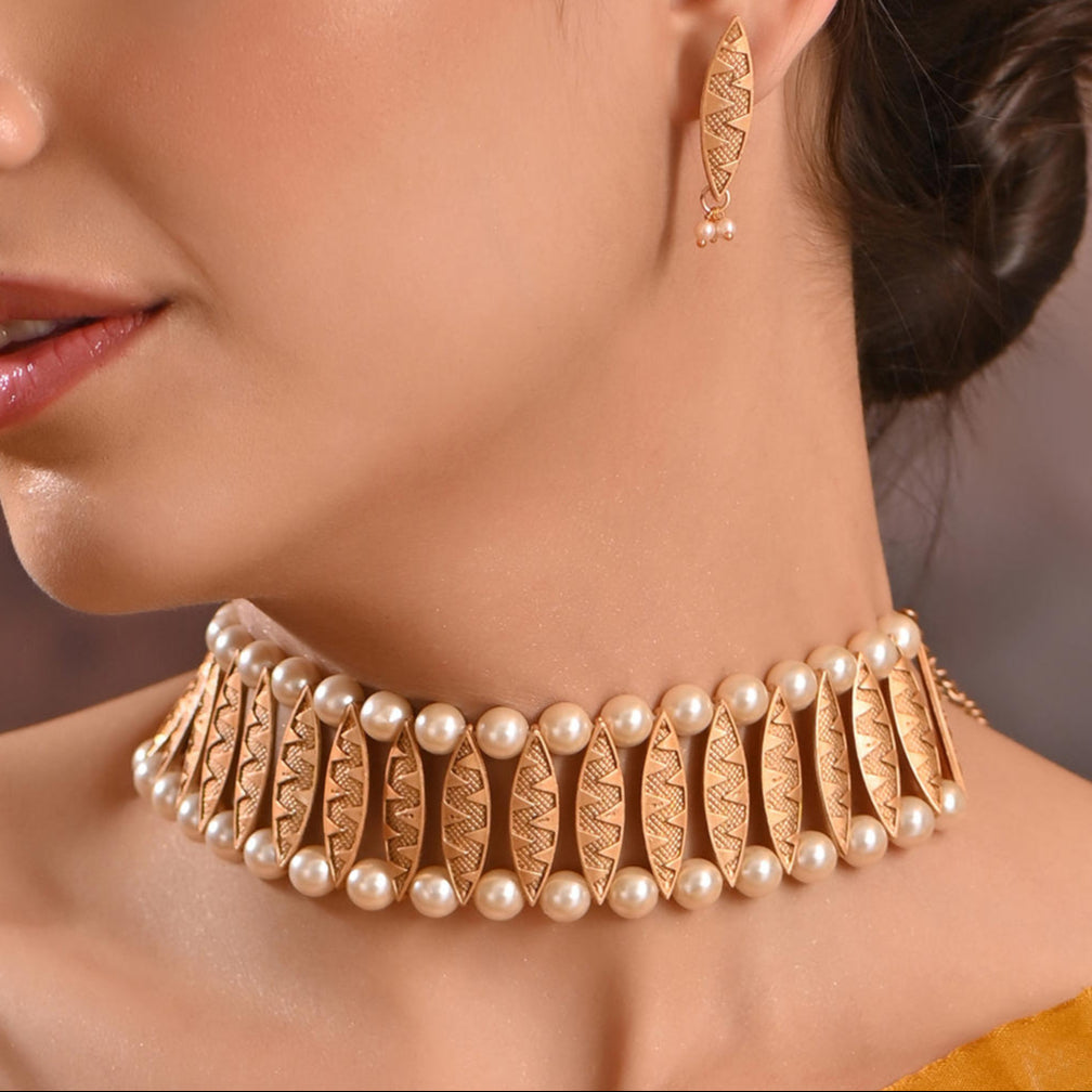 A woman wearing a gold-plated pearl choker necklace and matching earrings from the Fida brand. The jewelry features intricate gold detailing and lustrous pearls.