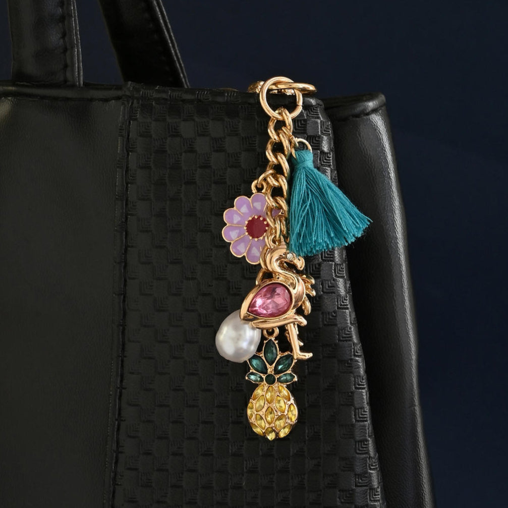 A gold-toned multicharm bag accessory with various charms including a tassel and enamel details, attached to a black handbag.