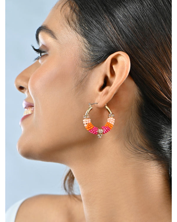 A woman wearing vibrant multicolored beaded hoop earrings with gold accents.