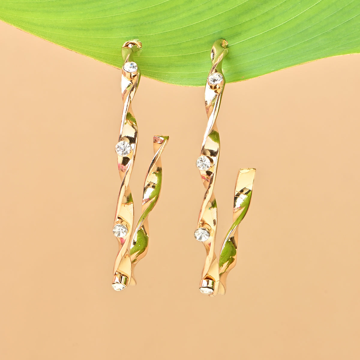 Gold earrings with diamond-like stones on a beige and green leaf background. ToniQ jewellery is skin safe, nickel free, cadmium free, hypoallergenic, and lab tested for your comfort and trust.