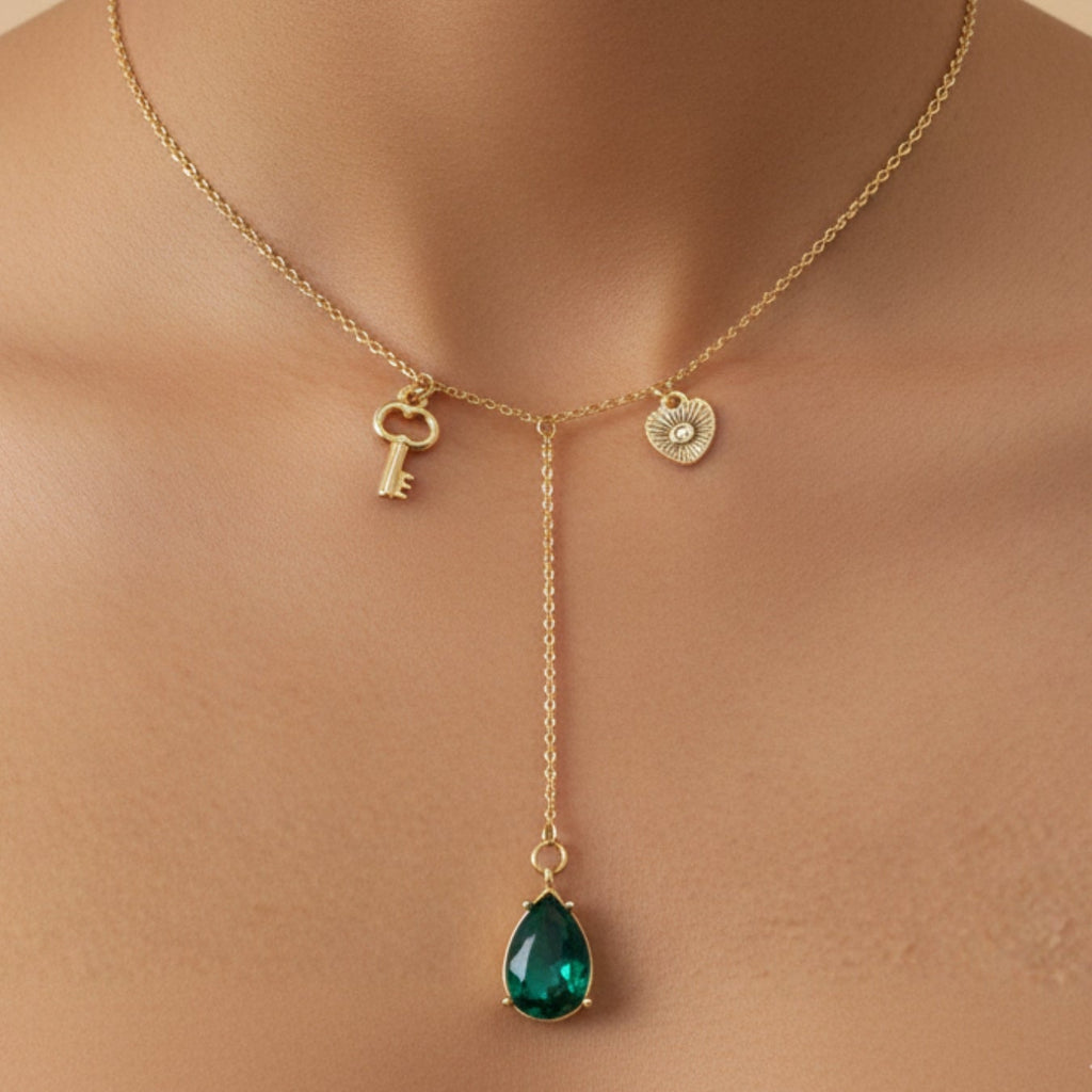 Gold necklace with a green teardrop pendant on a beige background