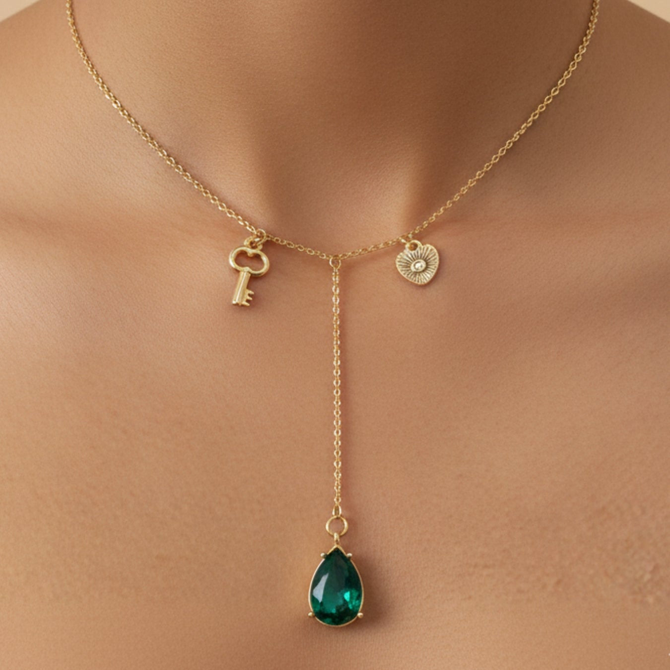 Gold necklace with a green teardrop pendant on a beige background