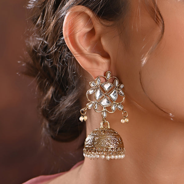 A person wearing a gold-plated floral jhumka earring with intricate designs and small pearl drops.