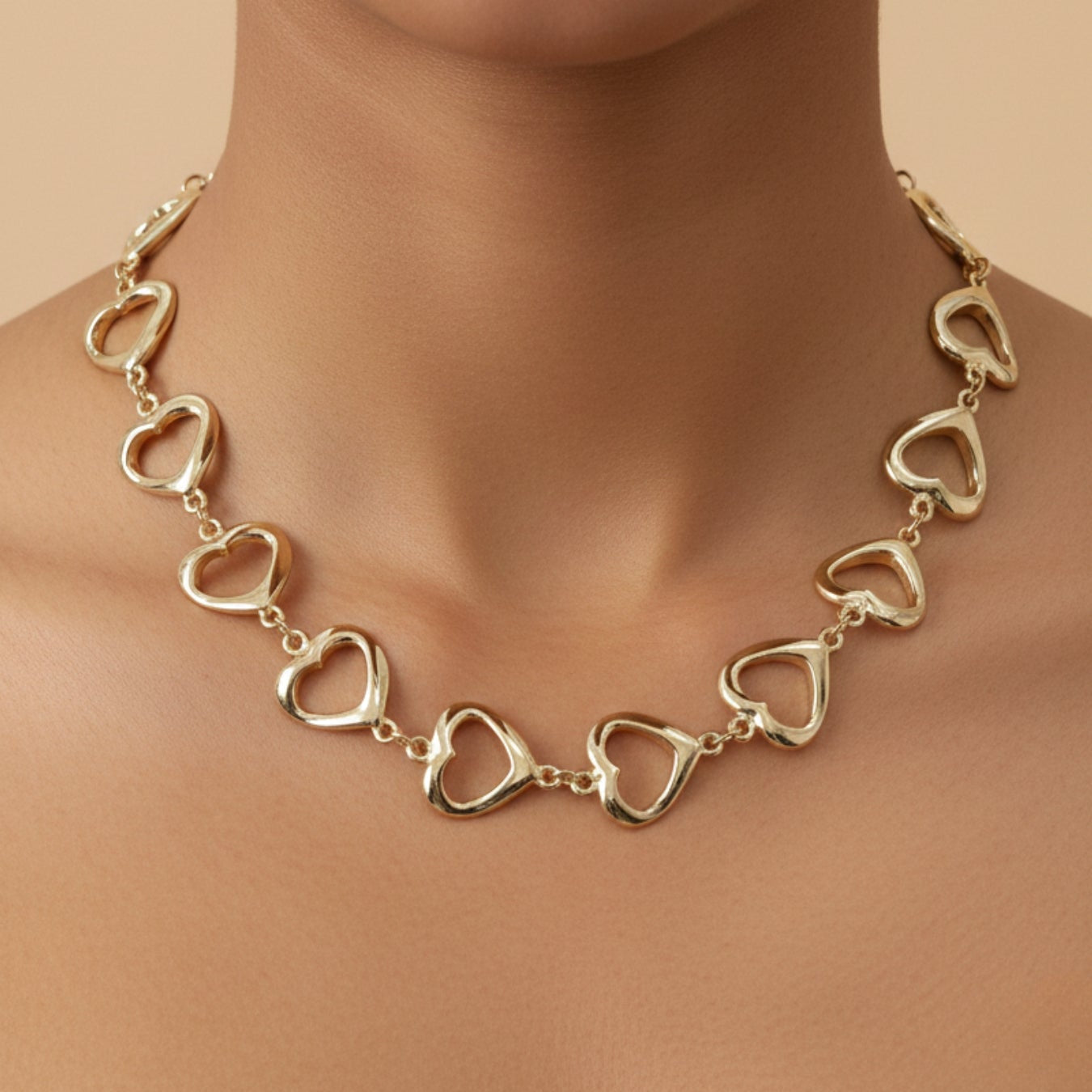 Gold heart-shaped necklace on a model against a beige background