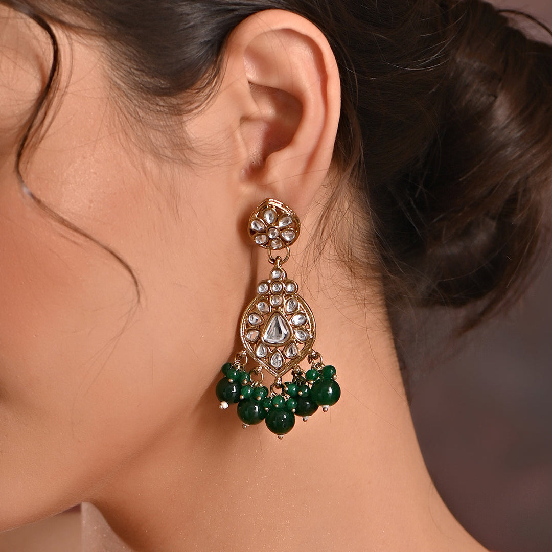 A pair of golden drop earrings with kundan stones and green beads