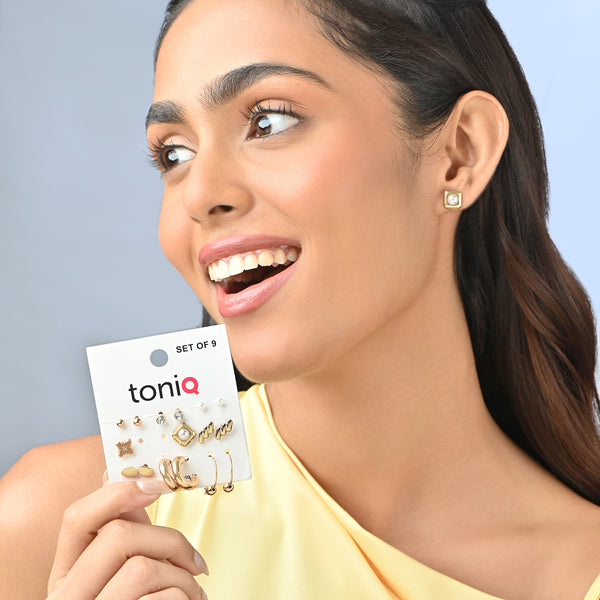 Woman wearing gold earrings and holding a toniq earring set packaging against a light blue background. ToniQ jewellery is skin safe, nickel free, cadmium free, hypoallergenic, and lab tested for your comfort and trust.