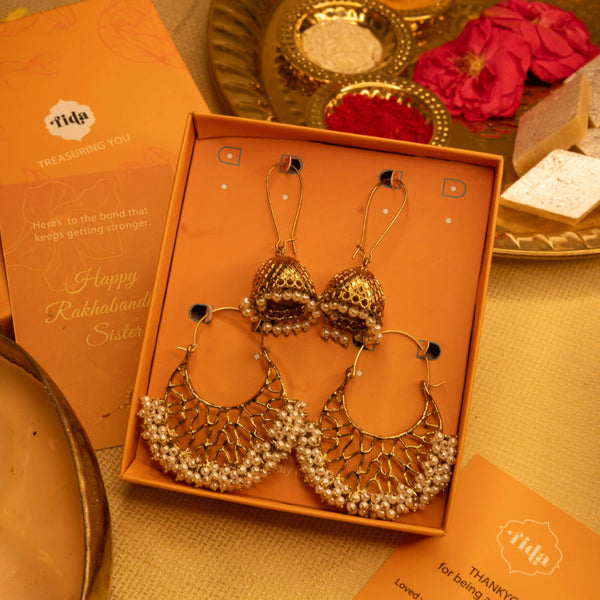 Gold earrings in an open box with a decorative tray and cards in the background