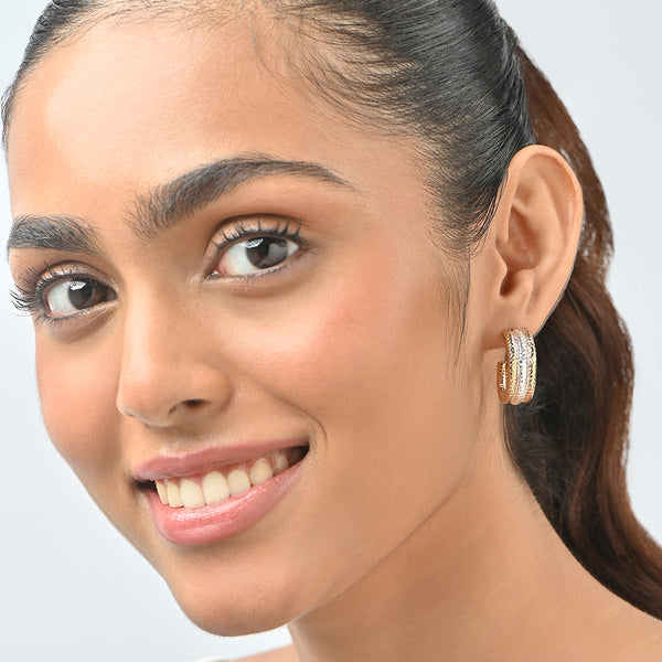 Close-up of a woman wearing gold hoop earrings on a light gray background