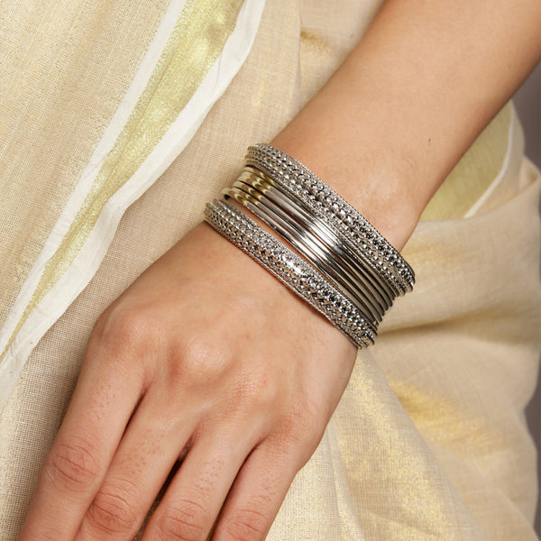 A women's wrist wearing multiple silver-plated beaded bangles with a variety of patterns.