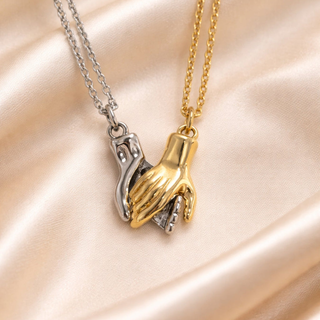 Two hand-shaped pendants on gold and silver chains against a beige satin background