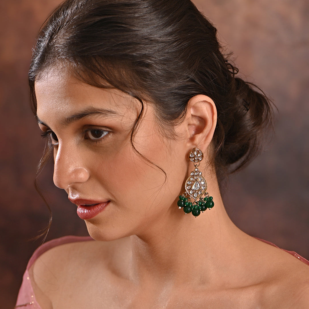 A pair of golden drop earrings with kundan stones and green beads