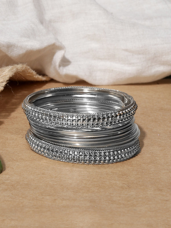 Stack of silver bangles on a brown surface with a white fabric background.