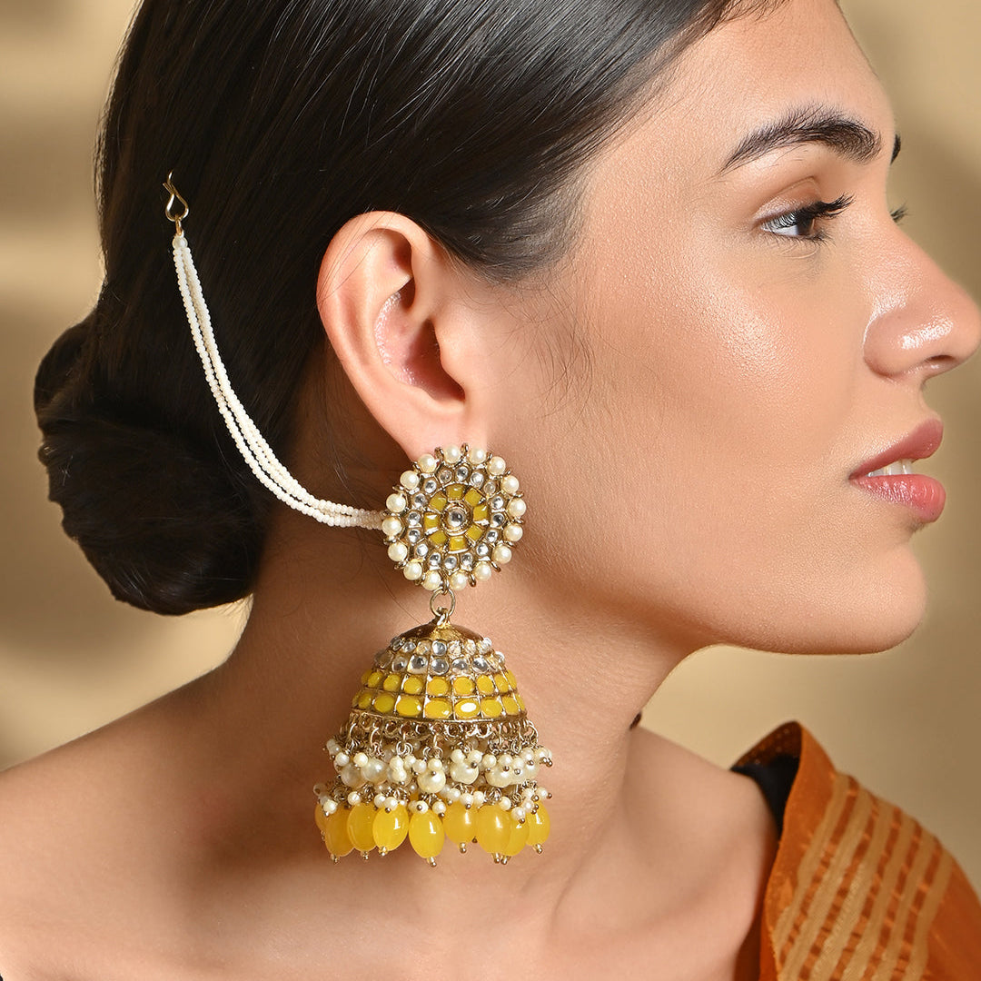 A woman wearing a gold-plated yellow bead kundan pearl jhumka earring with a floral design and a drop shape.
