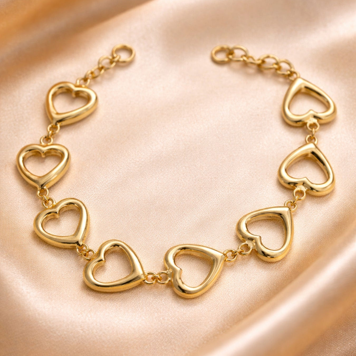 Gold heart-shaped bracelet on a soft pink fabric background