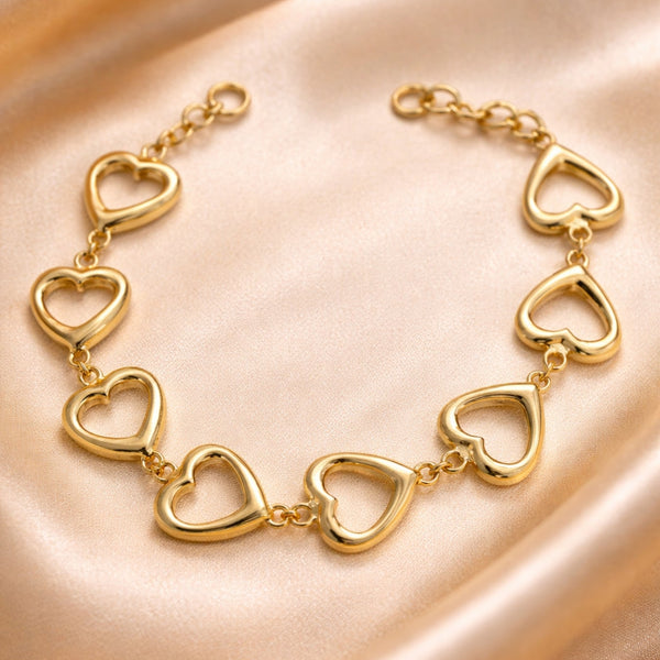 Gold heart-shaped bracelet on a soft pink fabric background