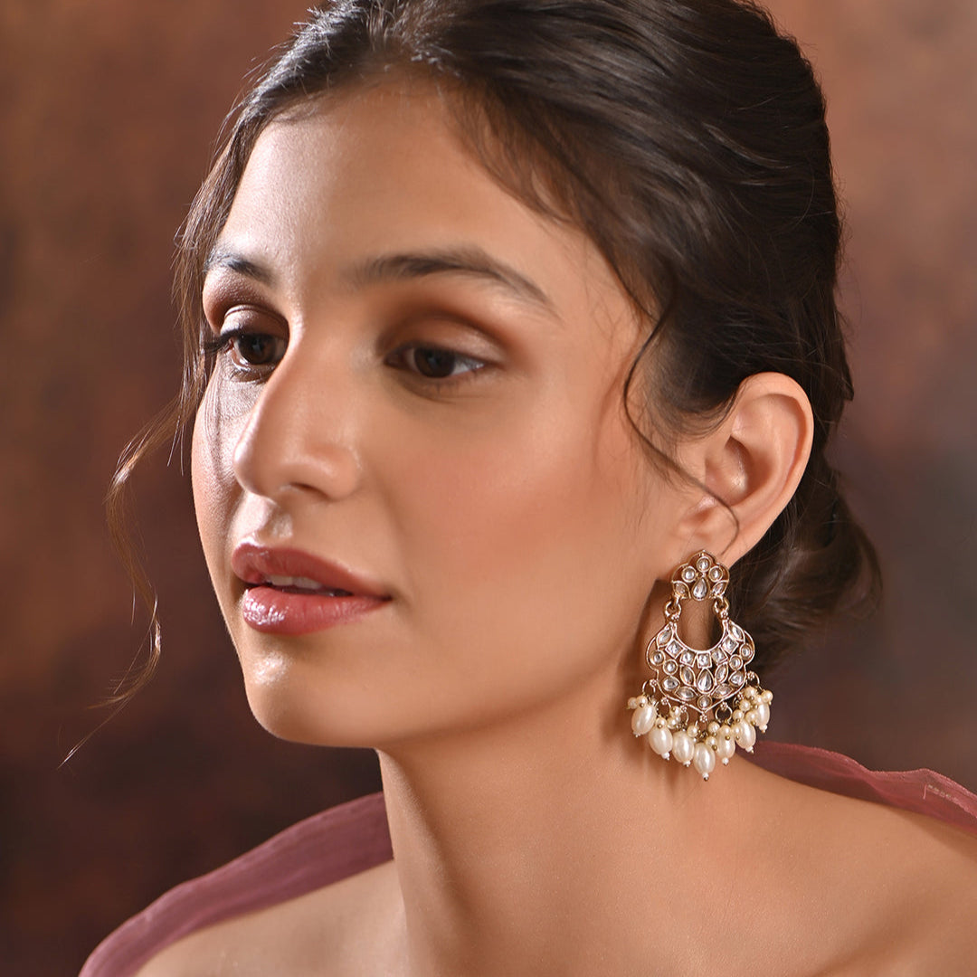A pair of gold-plated chandbali earrings adorned with white kundan stones and pearl drops