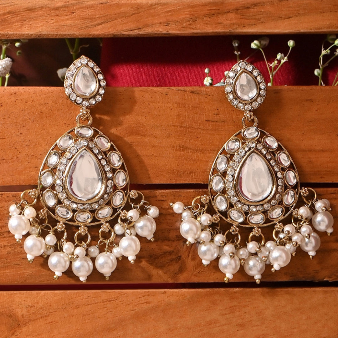 A pair of gold-plated ivory kundan stone drop earrings with ivory pearls, displayed against a wooden background.