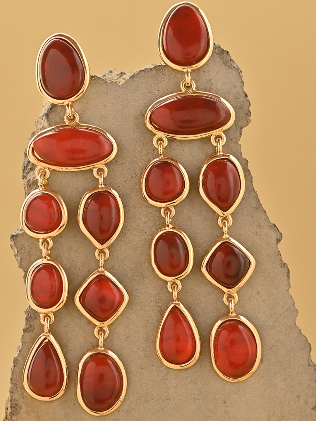 Gold earrings with red stones on a textured stone surface skin safe jewellery, nickel free, cadmium free, hypoallergenic, lab tested