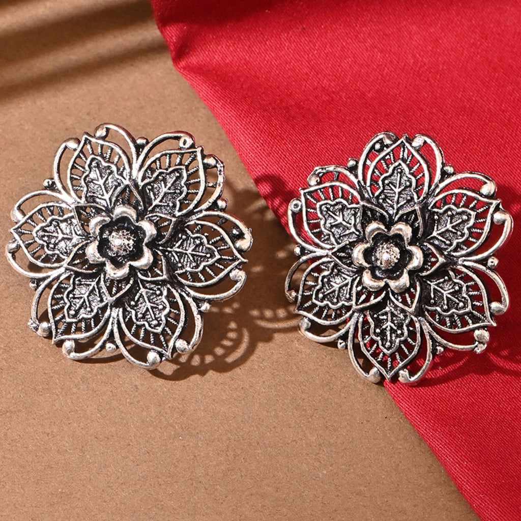 A pair of silver oxidised floral stud earrings displayed against a red and beige background.