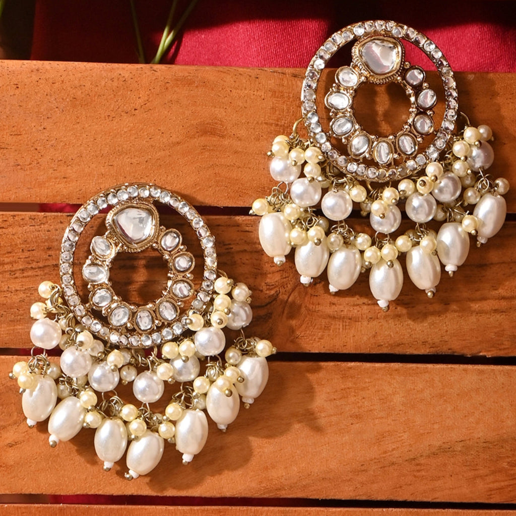 A pair of Radiant Kundan Round Drop Earrings with intricate kundan stonework and lustrous white pearls, set against a wooden background.