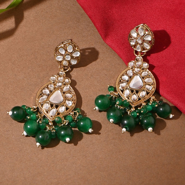 A pair of golden drop earrings with kundan stones and green beads against a brown and red background.