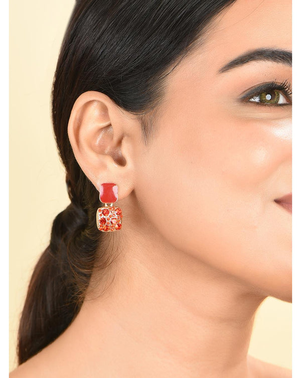 A woman wearing red gold plated geometric shape earrings with sparkling stones.