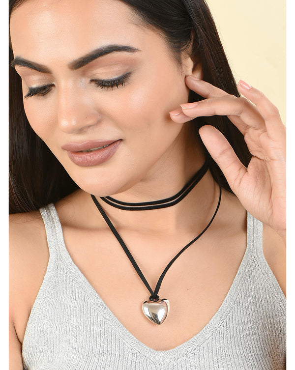 A woman wearing a white tank top and a long black silver-plated heart-shaped necklace.