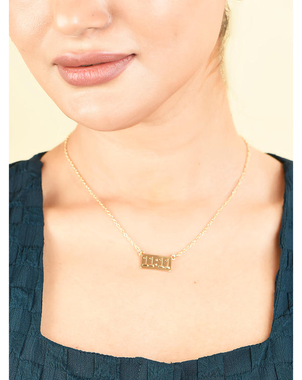 A woman wearing a green shirt and showcasing a gold plated pendant necklace with the number 11:11 engraved on it.