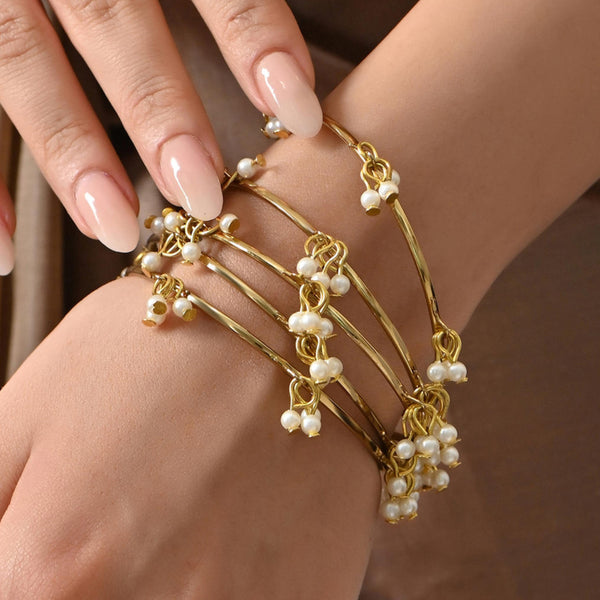 A gold-plated white pearl bangle worn on a person's wrist, featuring a slip-on closure and ornamental pearl drops.